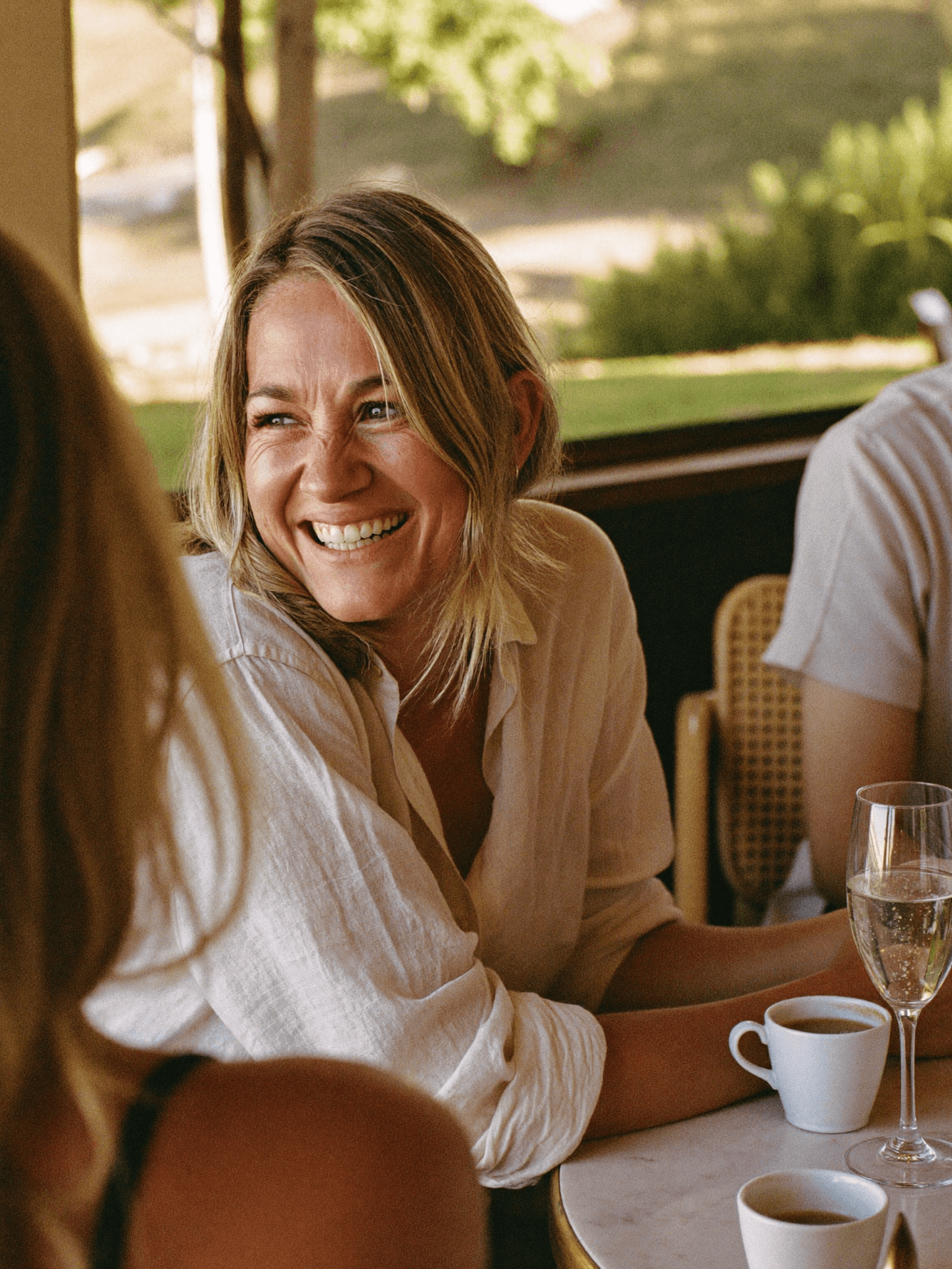 An Australian woman seated at a sunlit kitchen table holding a mug, mid-morning natural daylight